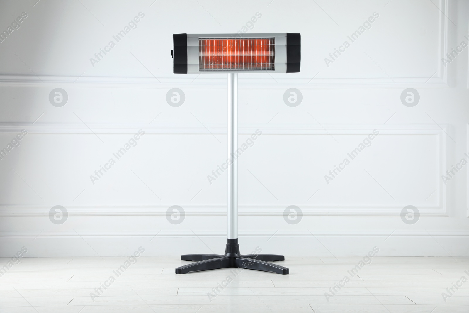 Photo of Electric infrared heater on floor near light grey wall indoors