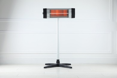 Photo of Electric infrared heater on floor near light grey wall indoors
