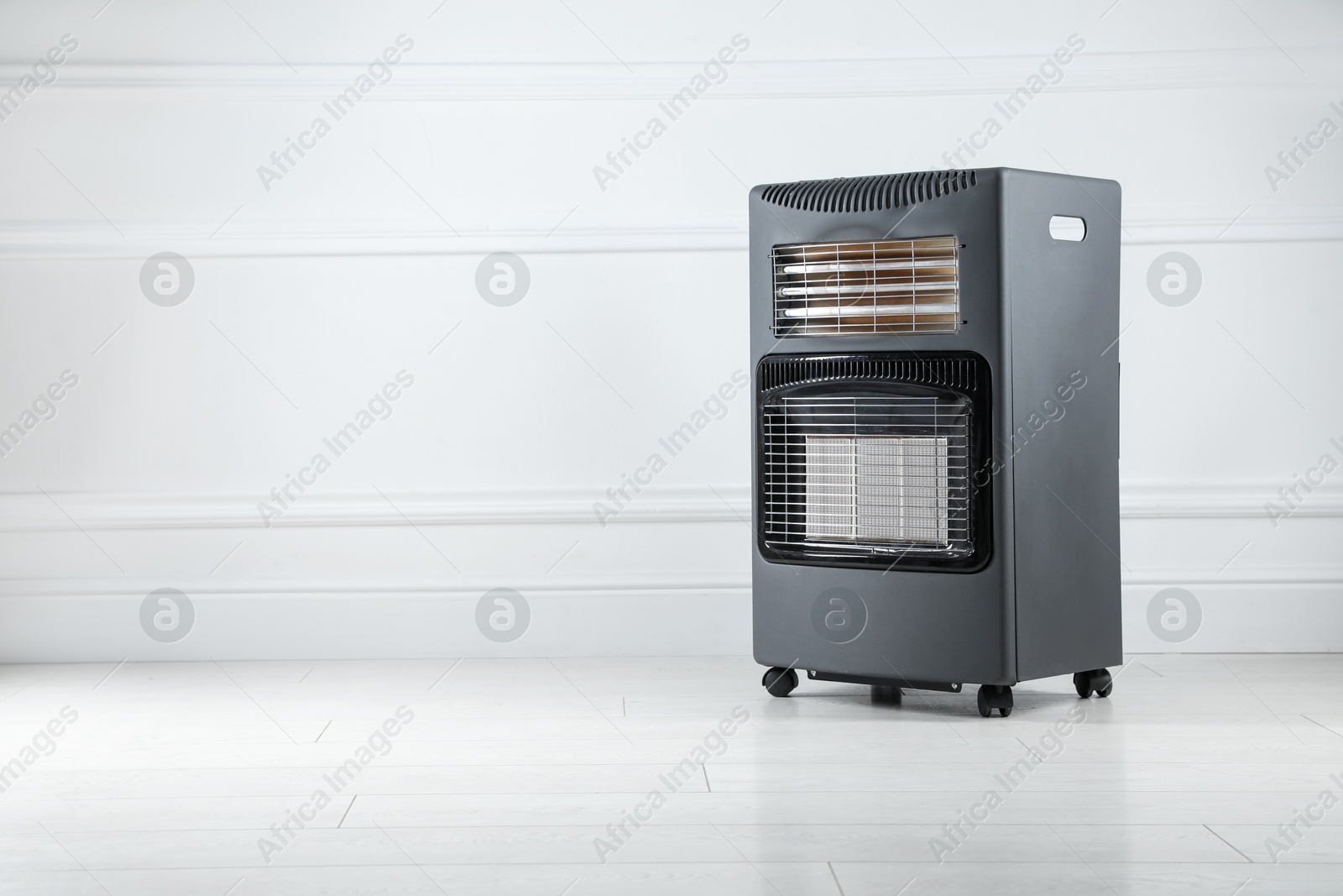 Photo of Electric heater on floor near light grey wall indoors. Space for text