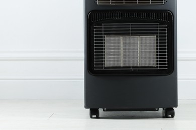 Photo of Electric heater on floor near light wall indoors, closeup. Space for text