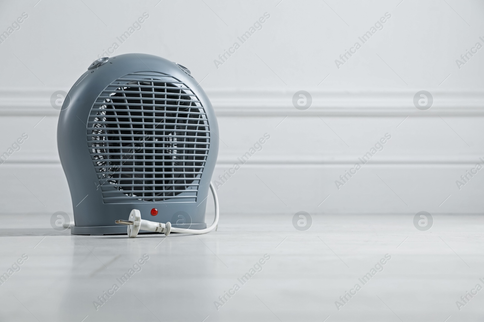 Photo of Electric fan heater on floor near light grey wall indoors, closeup. Space for text