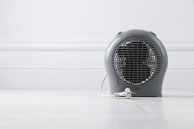 Photo of Electric fan heater on floor near light grey wall indoors, closeup. Space for text