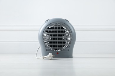 Photo of Electric fan heater on floor near light grey wall indoors, closeup