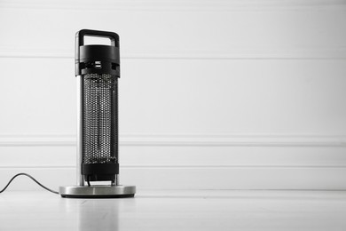 Photo of Electric heater on floor near light grey wall indoors. Space for text