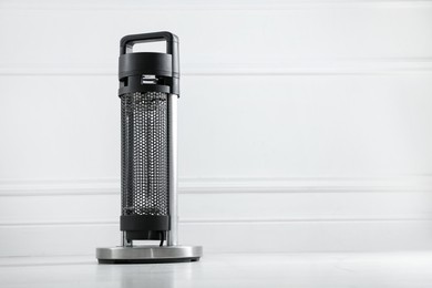 Photo of Electric heater on floor near light grey wall indoors. Space for text