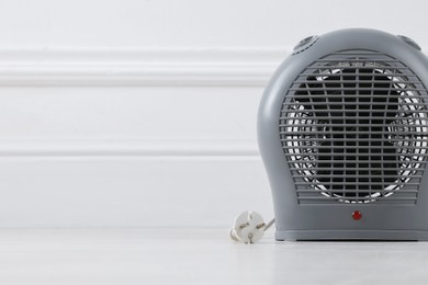 Photo of Electric fan heater on floor near light wall indoors, closeup. Space for text