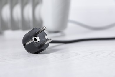 Photo of Electric plug of heater on light wooden floor, selective focus