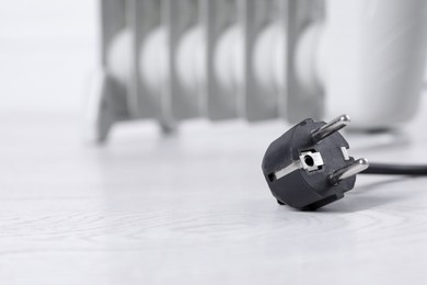 Photo of Electric plug of heater on light wooden floor, selective focus. Space for text
