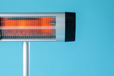 Photo of Electric infrared heater on light blue background, closeup. Space for text