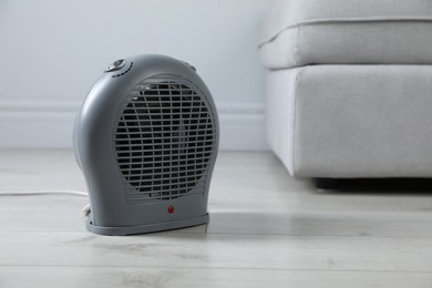 Photo of Electric fan heater on light wooden floor indoors, closeup. Space for text
