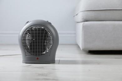 Photo of Electric fan heater on light wooden floor indoors. Space for text