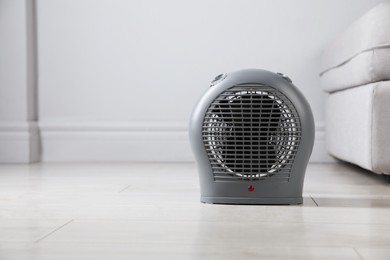 Photo of Electric fan heater on light wooden floor indoors. Space for text
