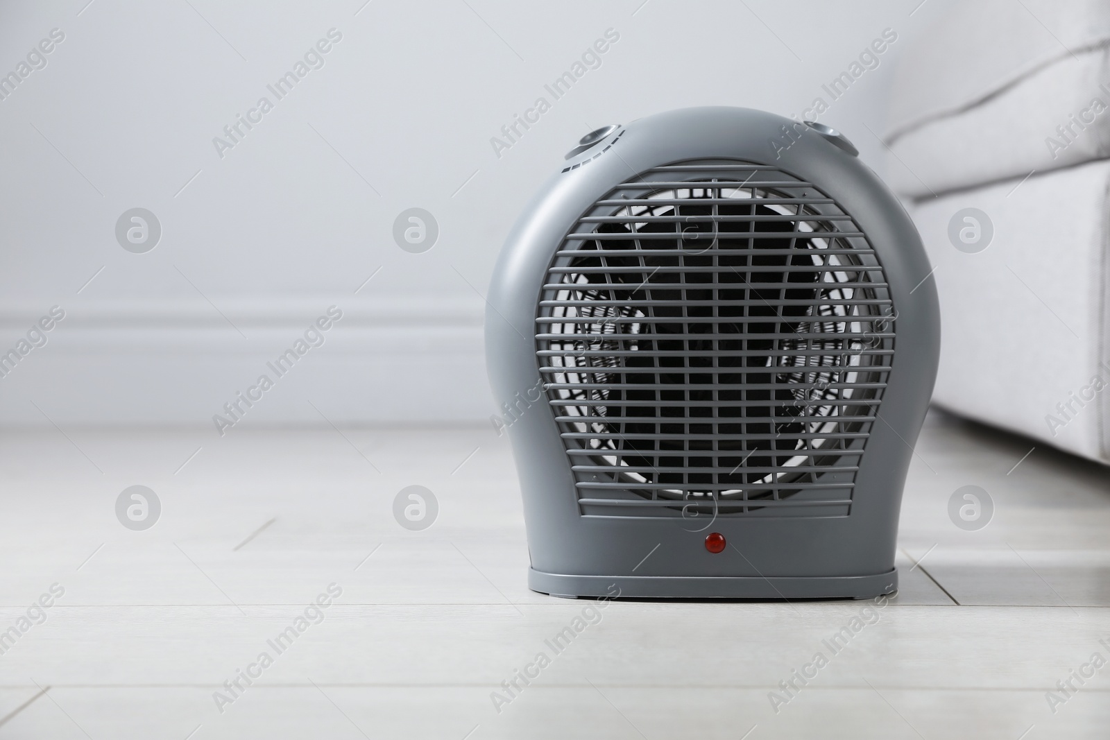 Photo of Electric fan heater on light wooden floor indoors, closeup. Space for text
