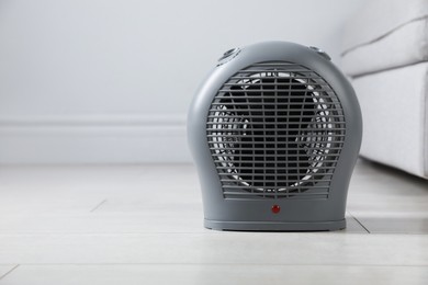 Photo of Electric fan heater on light wooden floor indoors, closeup. Space for text