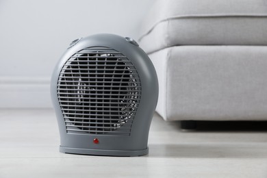 Photo of Electric fan heater on light wooden floor indoors, closeup. Space for text