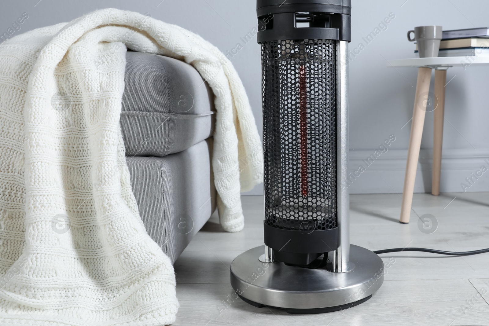 Photo of Electric heater and pouf with blanket on light wooden floor indoors, closeup