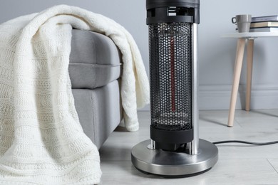 Photo of Electric heater and pouf with blanket on light wooden floor indoors, closeup