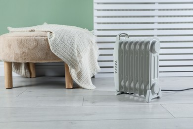 Photo of Electric heater and pouf with blanket on light wooden floor indoors