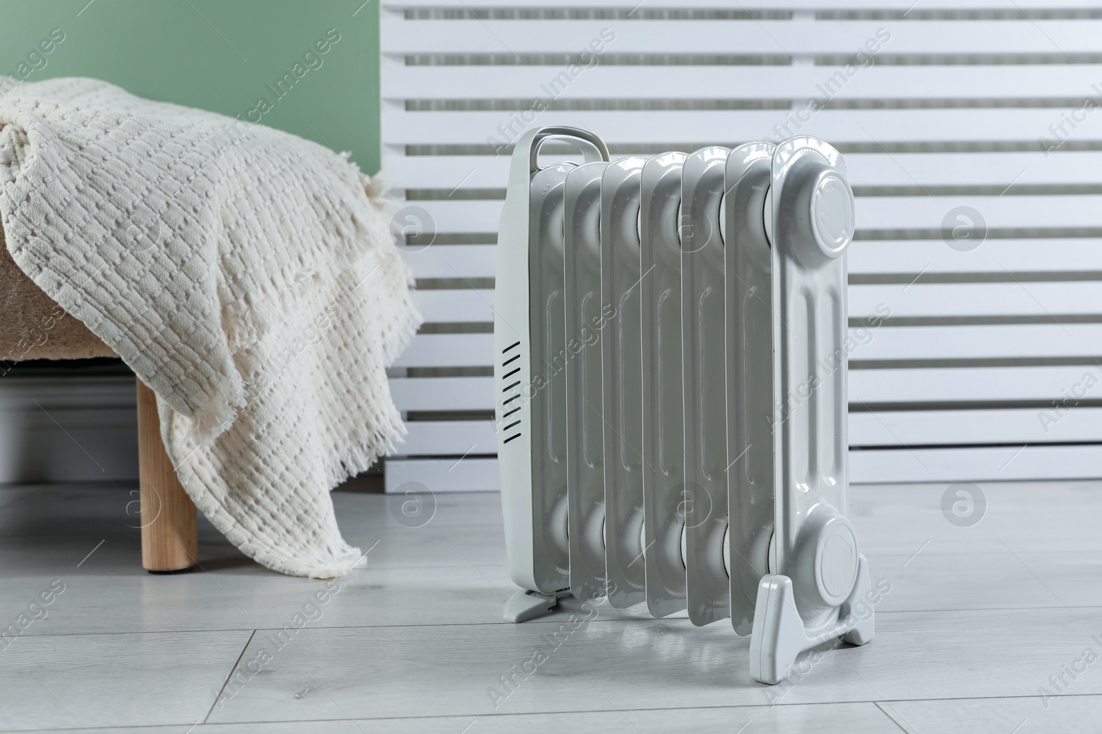 Photo of Electric heater and pouf with blanket on light wooden floor indoors