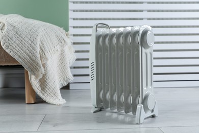 Photo of Electric heater and pouf with blanket on light wooden floor indoors
