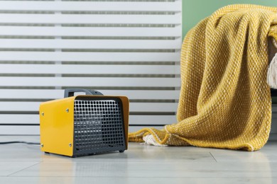 Photo of Electric fan heater and pouf with blanket on light wooden floor indoors