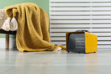 Photo of Electric fan heater and pouf with blanket on light wooden floor indoors