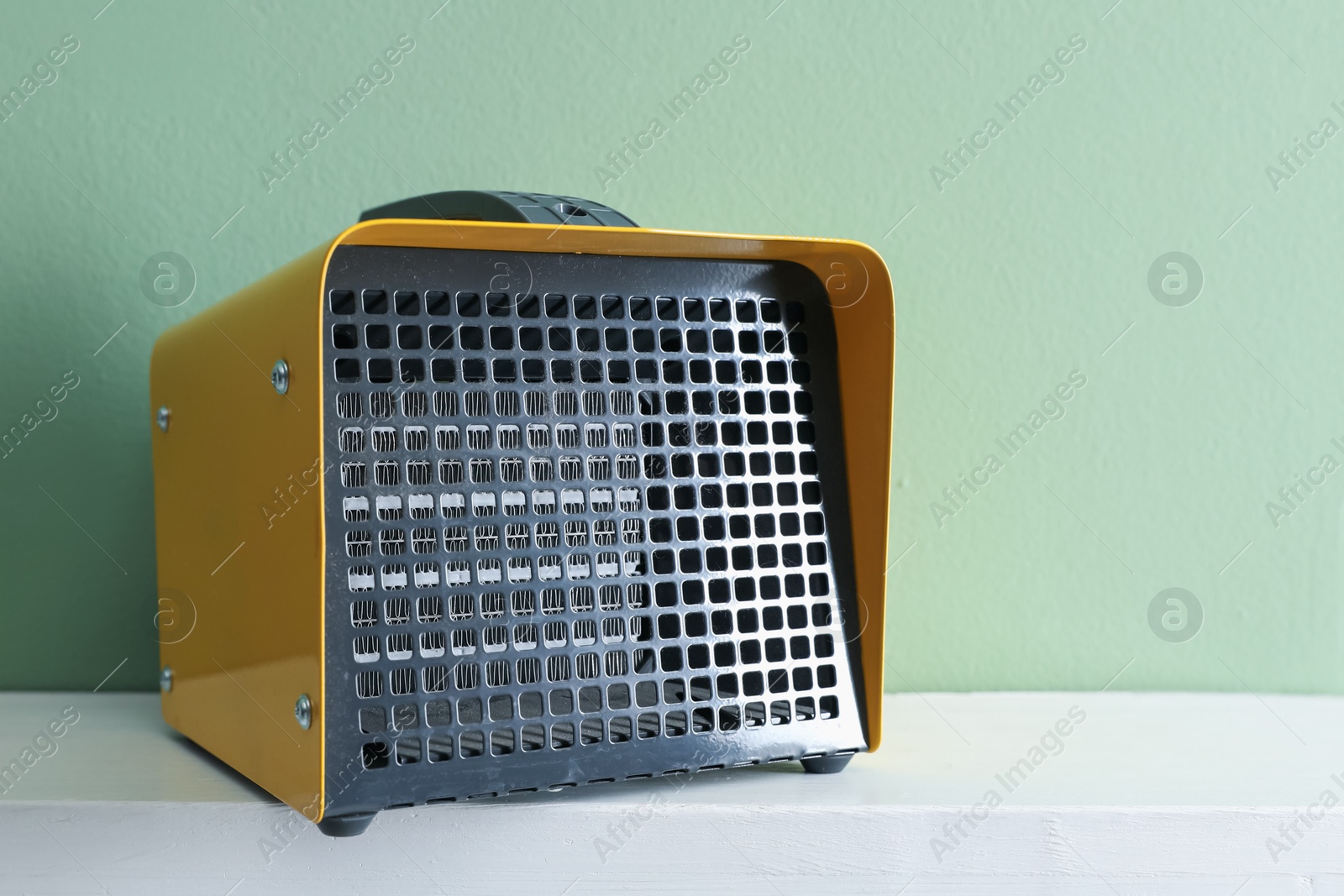 Photo of Electric fan heater on white counter near green wall indoors, closeup. Space for text