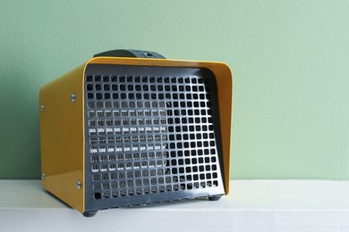 Photo of Electric fan heater on white counter near green wall indoors, closeup. Space for text
