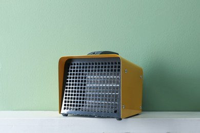 Photo of Electric fan heater on white counter near green wall indoors, closeup