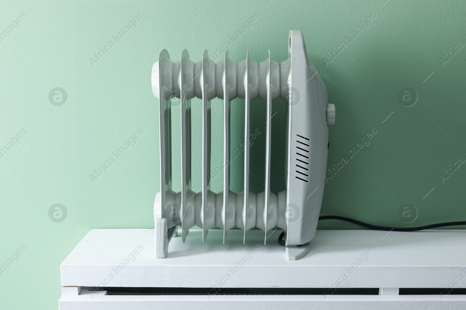 Photo of Electric heater on white radiator near green wall indoors