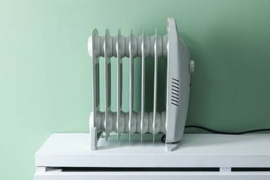 Photo of Electric heater on white radiator near green wall indoors
