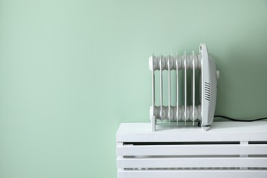 Photo of Electric heater on white radiator near green wall indoors. Space for text