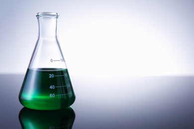 Photo of Flask with green liquid on table against white background. Space for text