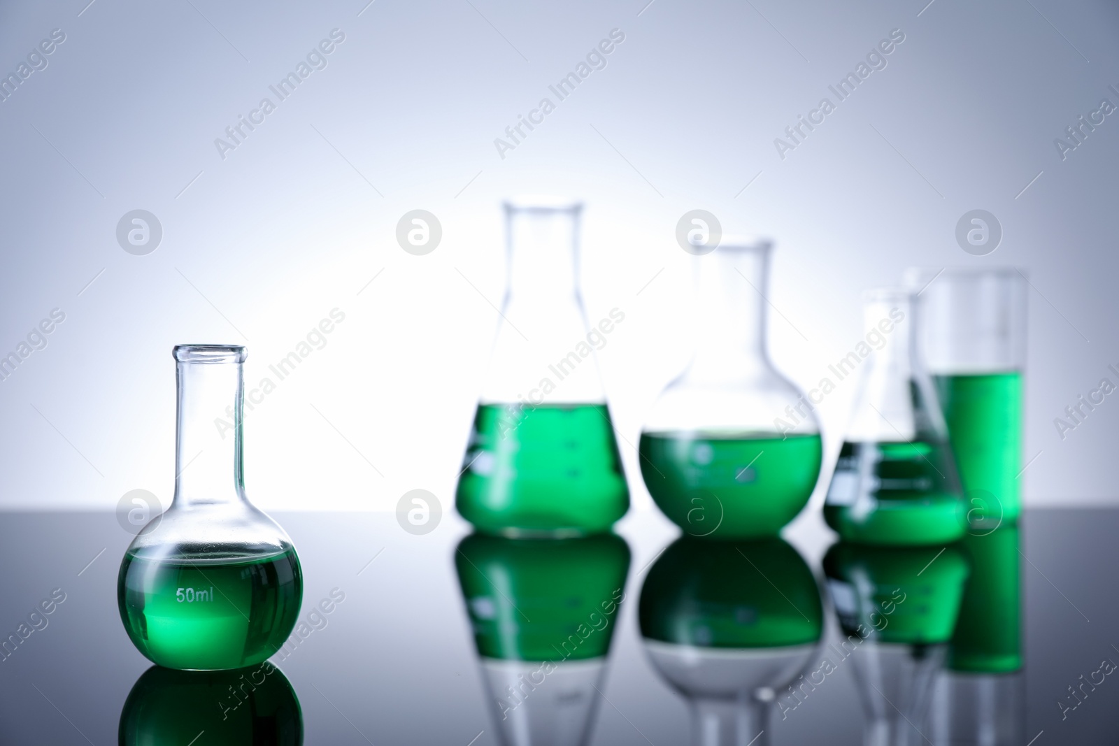 Photo of Different laboratory glassware with green liquid on table against white background