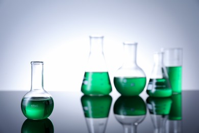 Photo of Different laboratory glassware with green liquid on table against white background