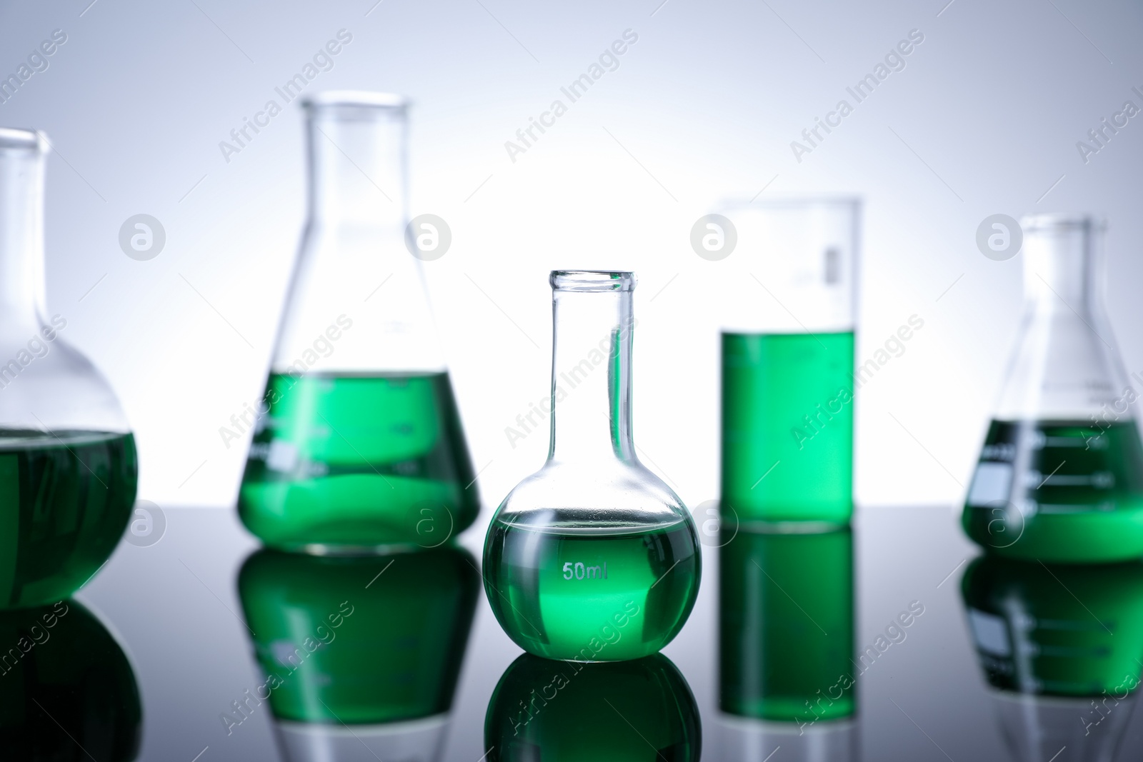 Photo of Different laboratory glassware with green liquid on table against white background