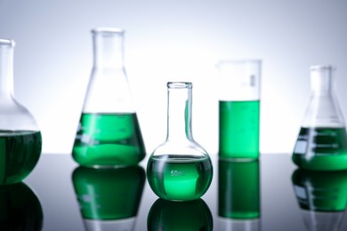 Photo of Different laboratory glassware with green liquid on table against white background