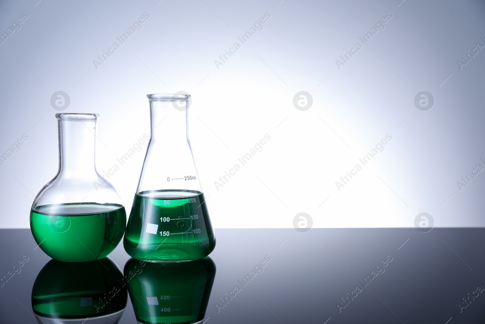 Photo of Different laboratory glassware with green liquid on table against white background. Space for text