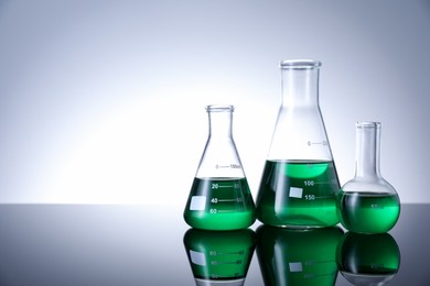 Photo of Different laboratory glassware with green liquid on table against white background. Space for text
