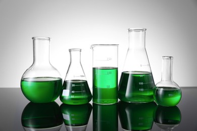 Photo of Different laboratory glassware with green liquid on table against white background