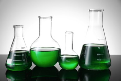 Photo of Different laboratory glassware with green liquid on table against white background