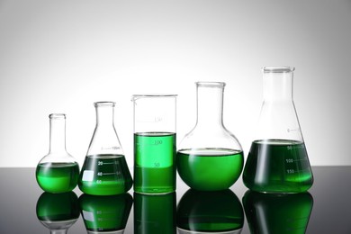 Photo of Different laboratory glassware with green liquid on table against white background