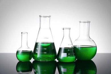Photo of Different laboratory glassware with green liquid on table against white background