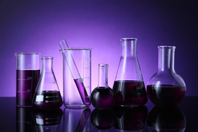 Photo of Different laboratory glassware with color liquid on table against violet background