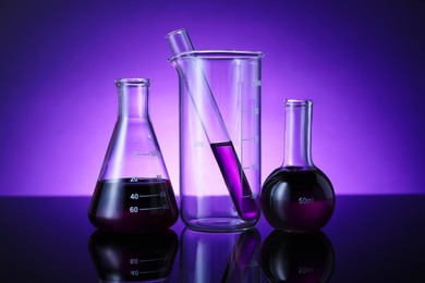 Photo of Different laboratory glassware with color liquid on table against violet background