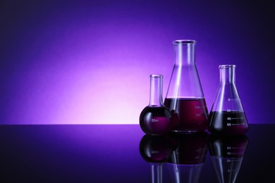 Photo of Different laboratory glassware with color liquid on table against violet background. Space for text