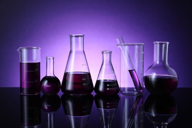 Photo of Different laboratory glassware with color liquid on table against violet background
