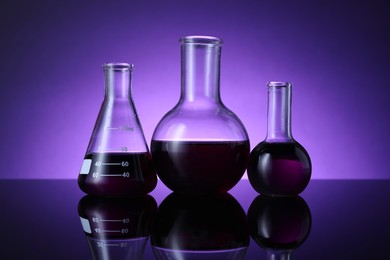 Photo of Different laboratory glassware with color liquid on table against violet background