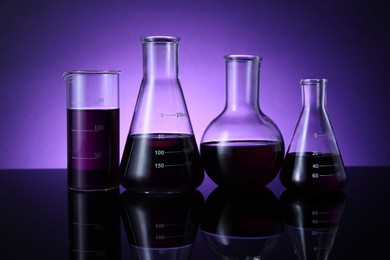 Photo of Different laboratory glassware with color liquid on table against violet background