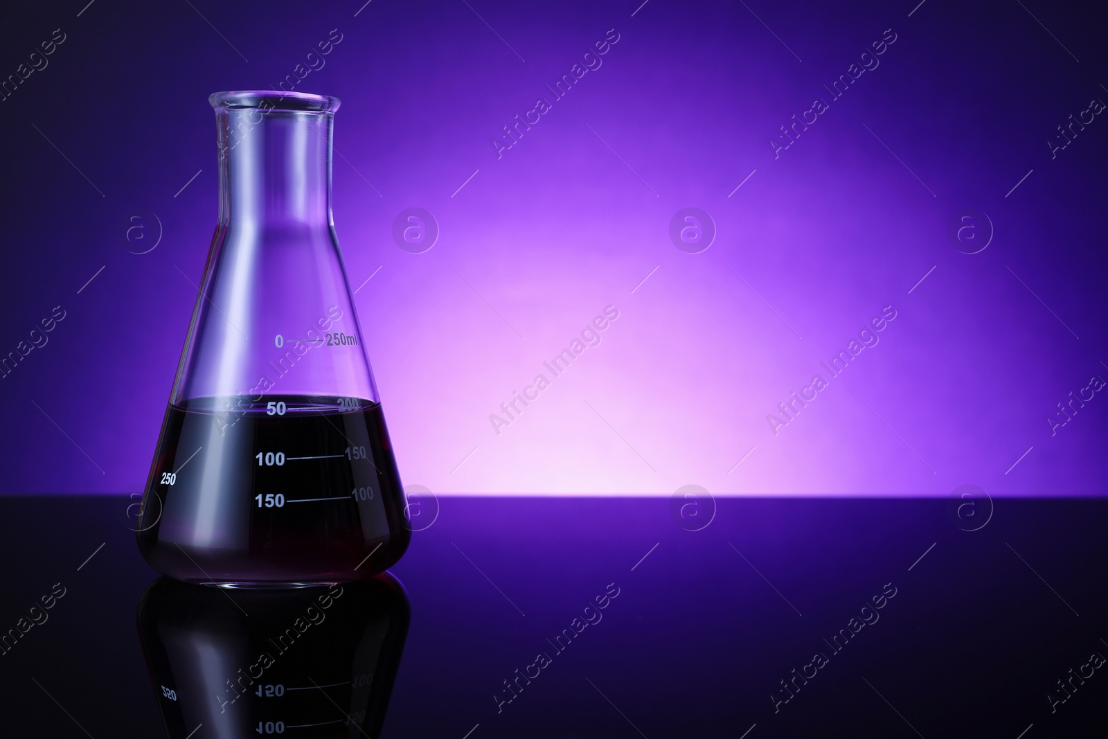 Photo of Flask with color liquid on table against violet background. Space for text